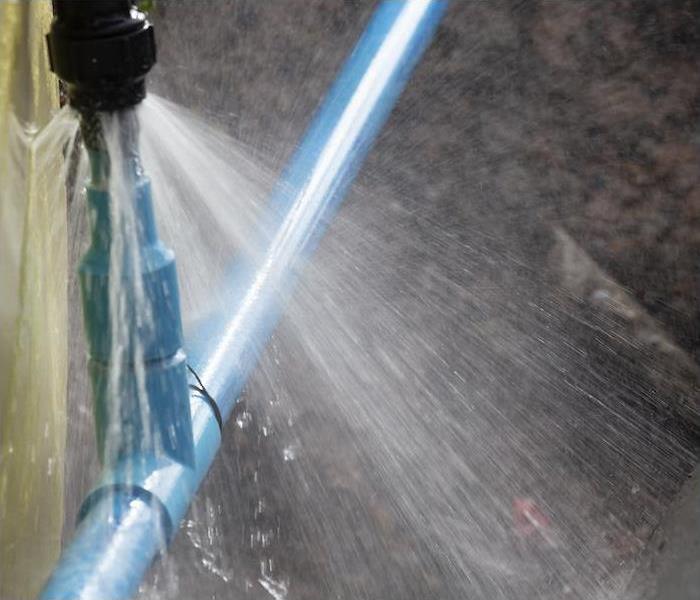 water spraying out of blue plumbing pipes due to a leak