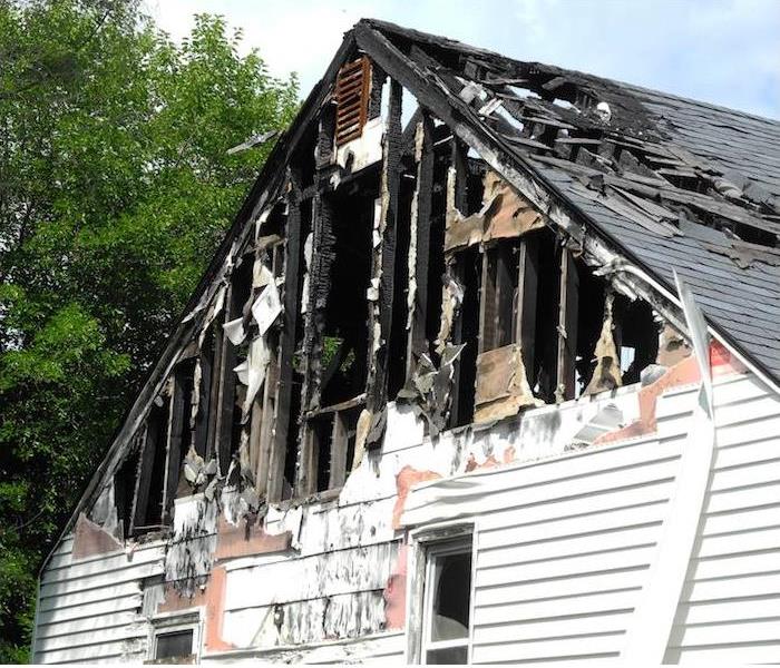 a small white house showing signs major damage from a recent fire
